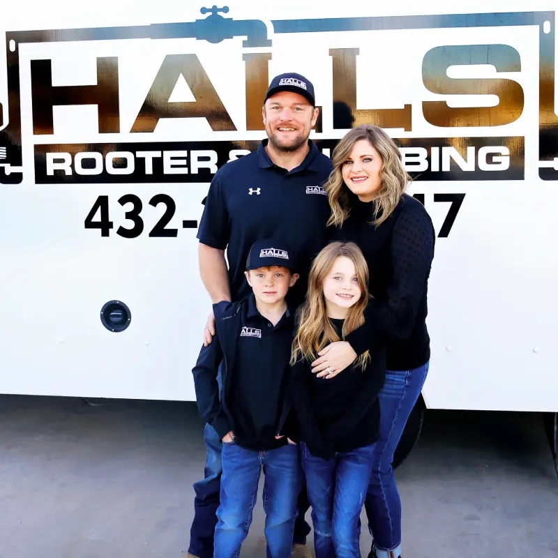 A man, woman, and two children stand smiling in front of a truck labeled "Halls Rooter & Plumbing.